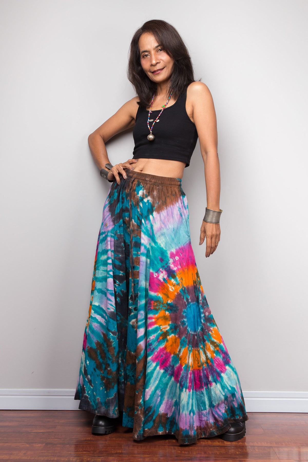 Woman standing with hand on hip wearing Nuichan teal spiral tie dye wide leg palazzo pants, front view showing the full mandala pattern radiating from the waist to the hem