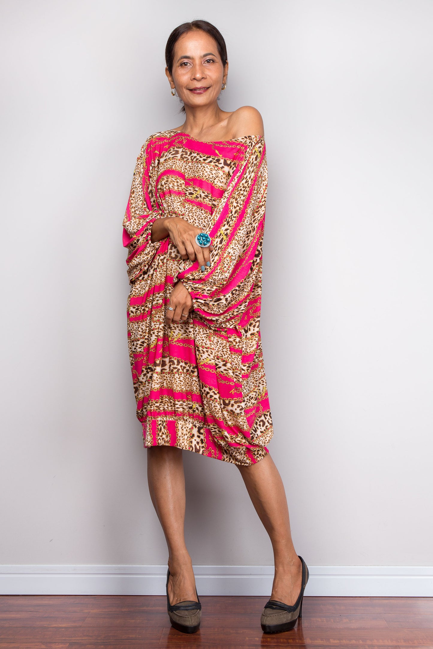 Woman wearing a patterned  tunic kaftan dress with pink and gold design against a plain background