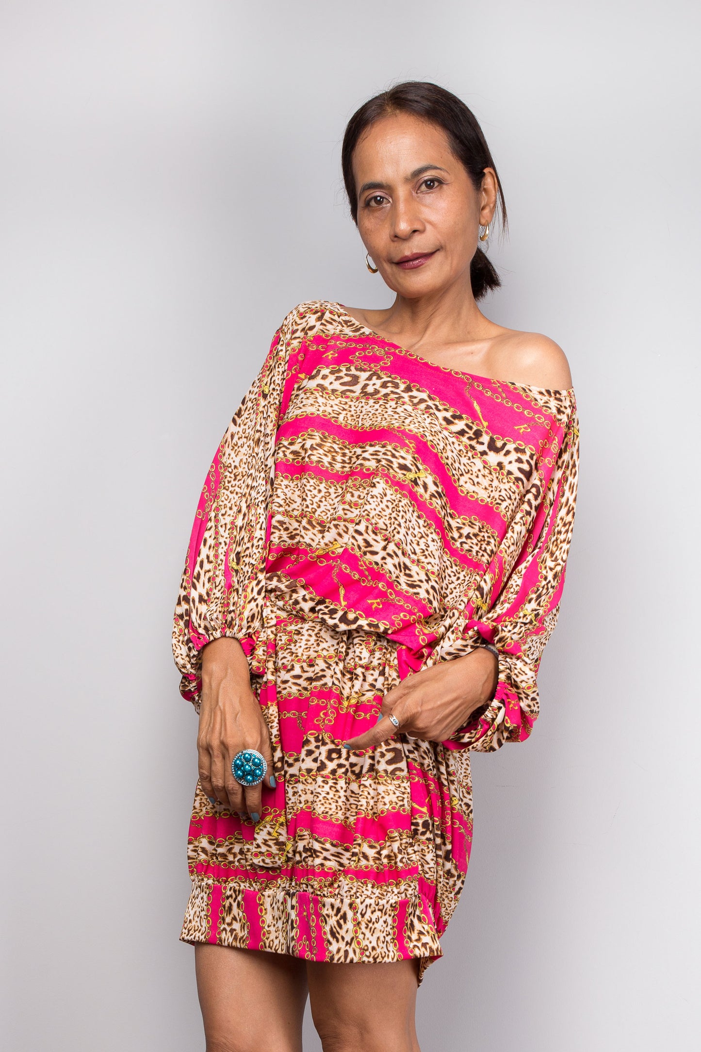 Petite Woman wearing a patterned tunic kaftan dress with pink and gold design on a plain background