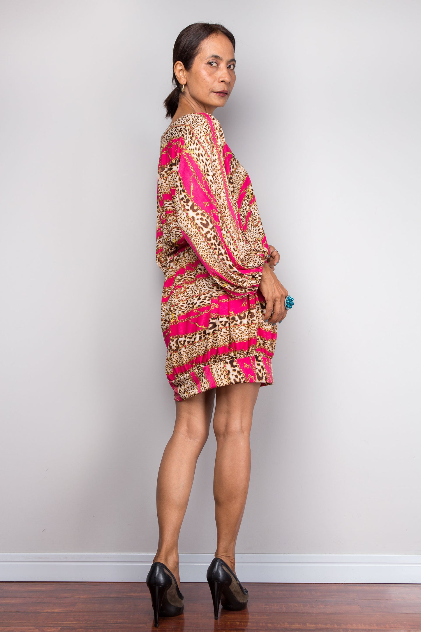 Woman wearing a patterned dress with pink and gold accents against a plain background