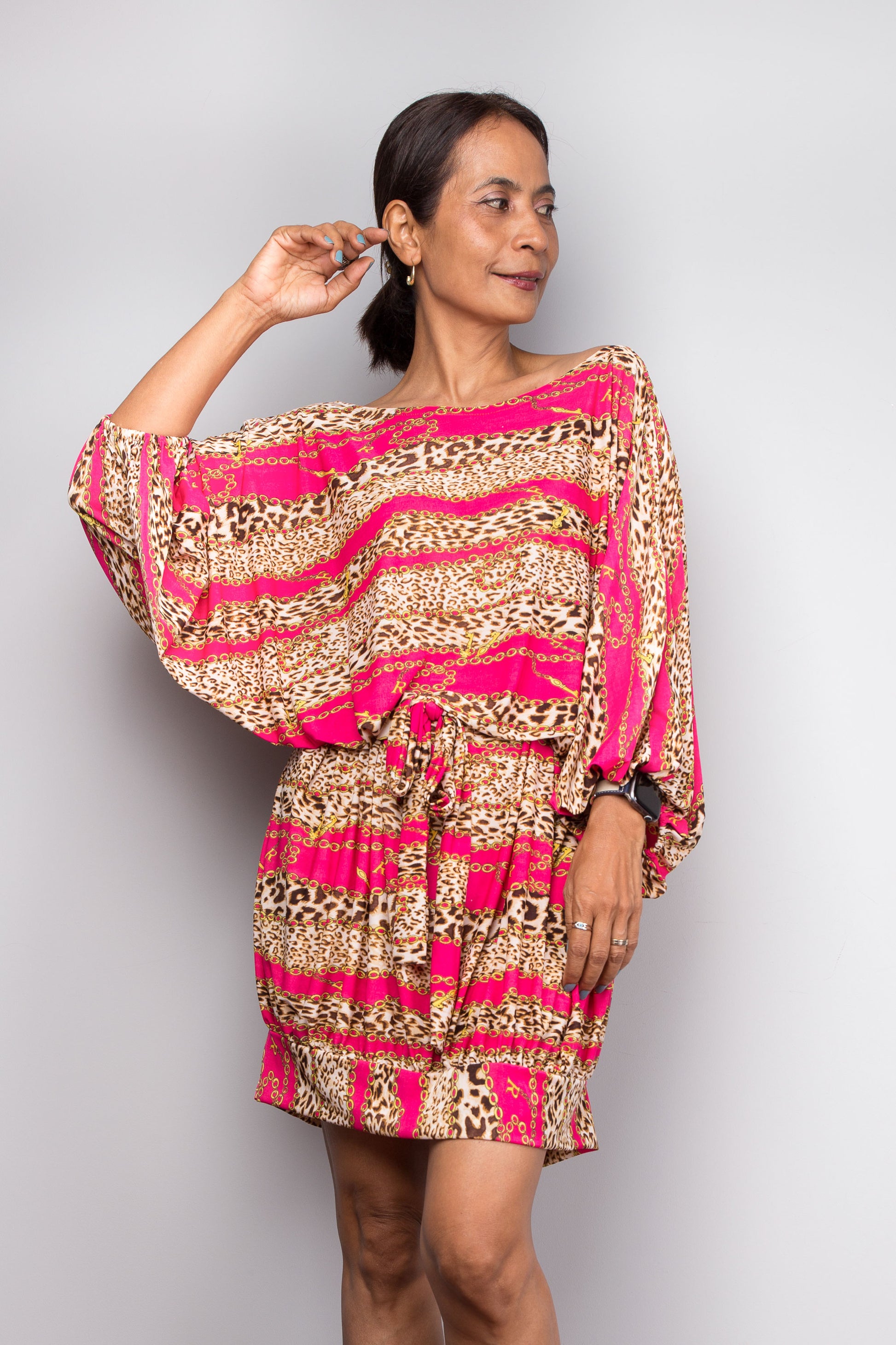 Woman wearing a colorful petite tunic dress with pink and gold patterns on a plain background