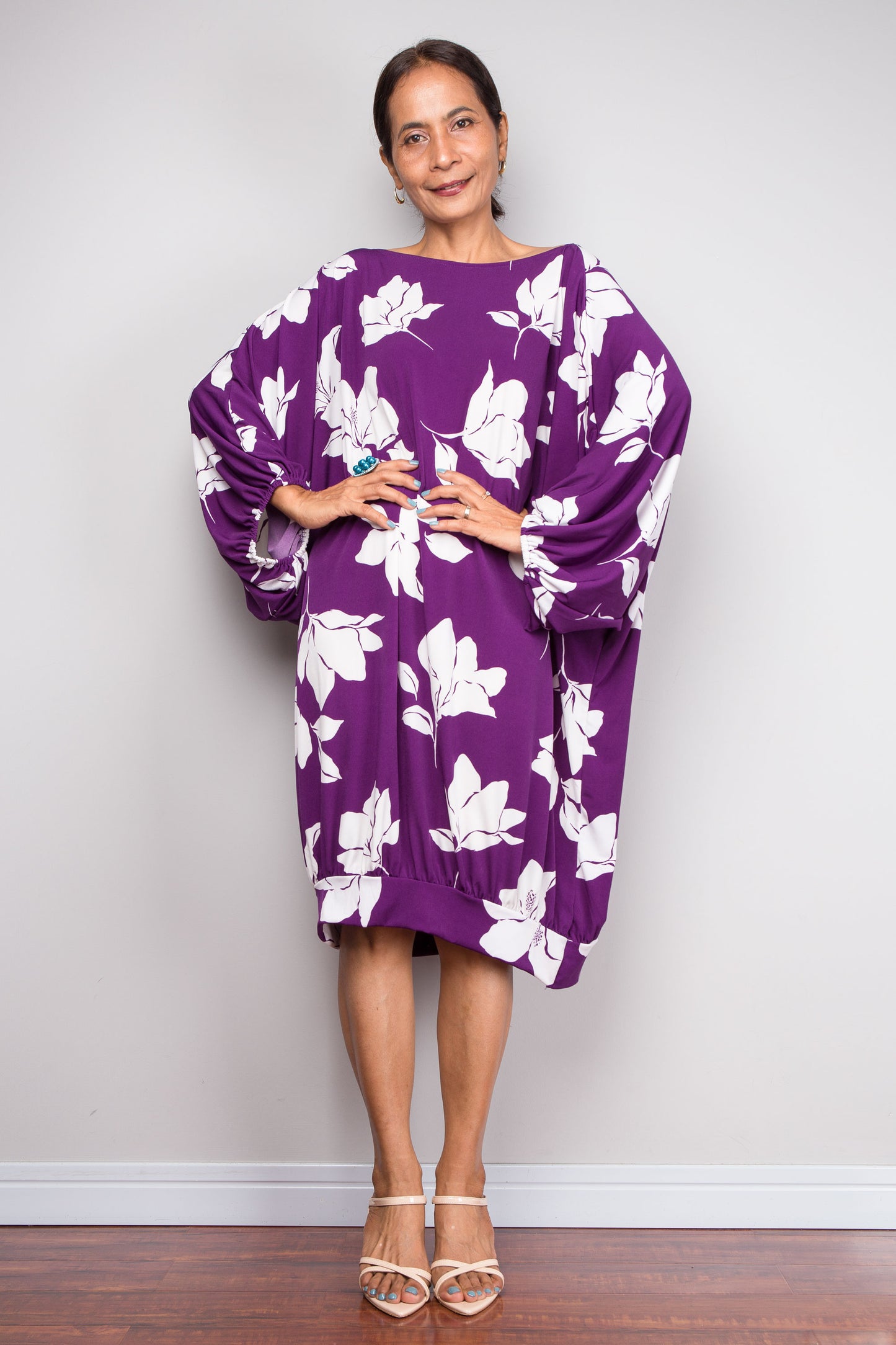 Woman wearing a vivid purple tunic dress with white floral patterns against a plain background