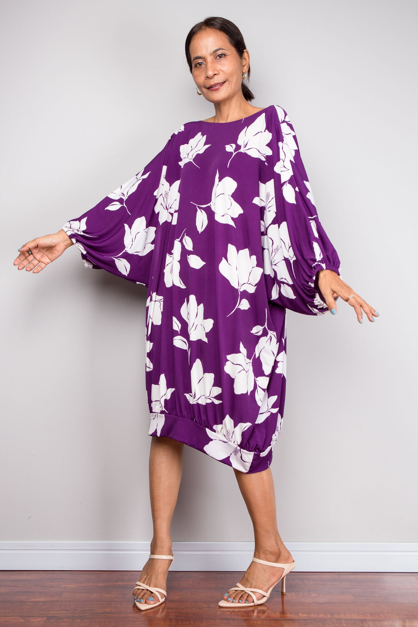 Woman wearing a purple tunic dress with white floral patterns against a plain background