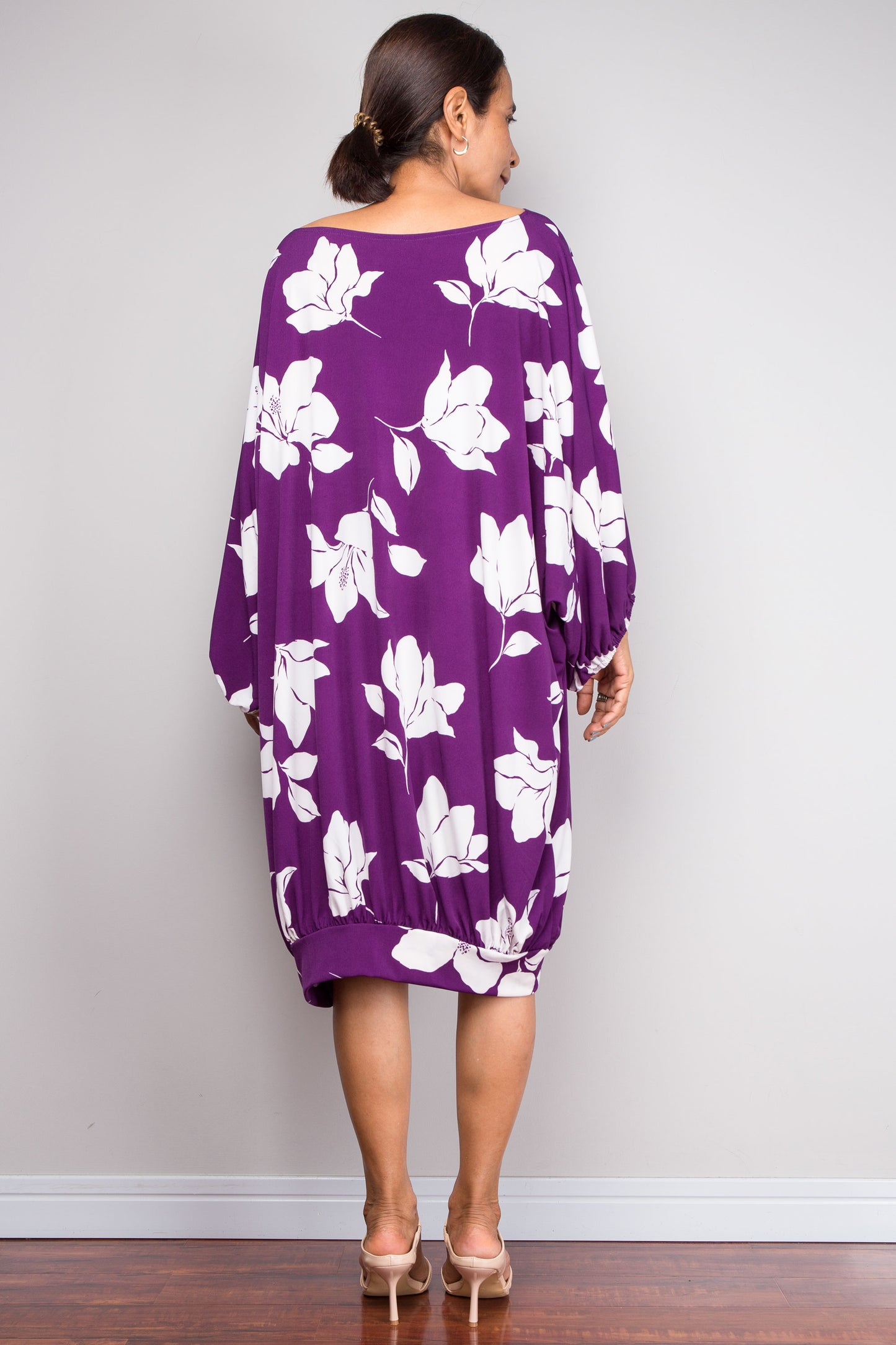 Woman wearing a purple dress with white floral patterns against a plain background