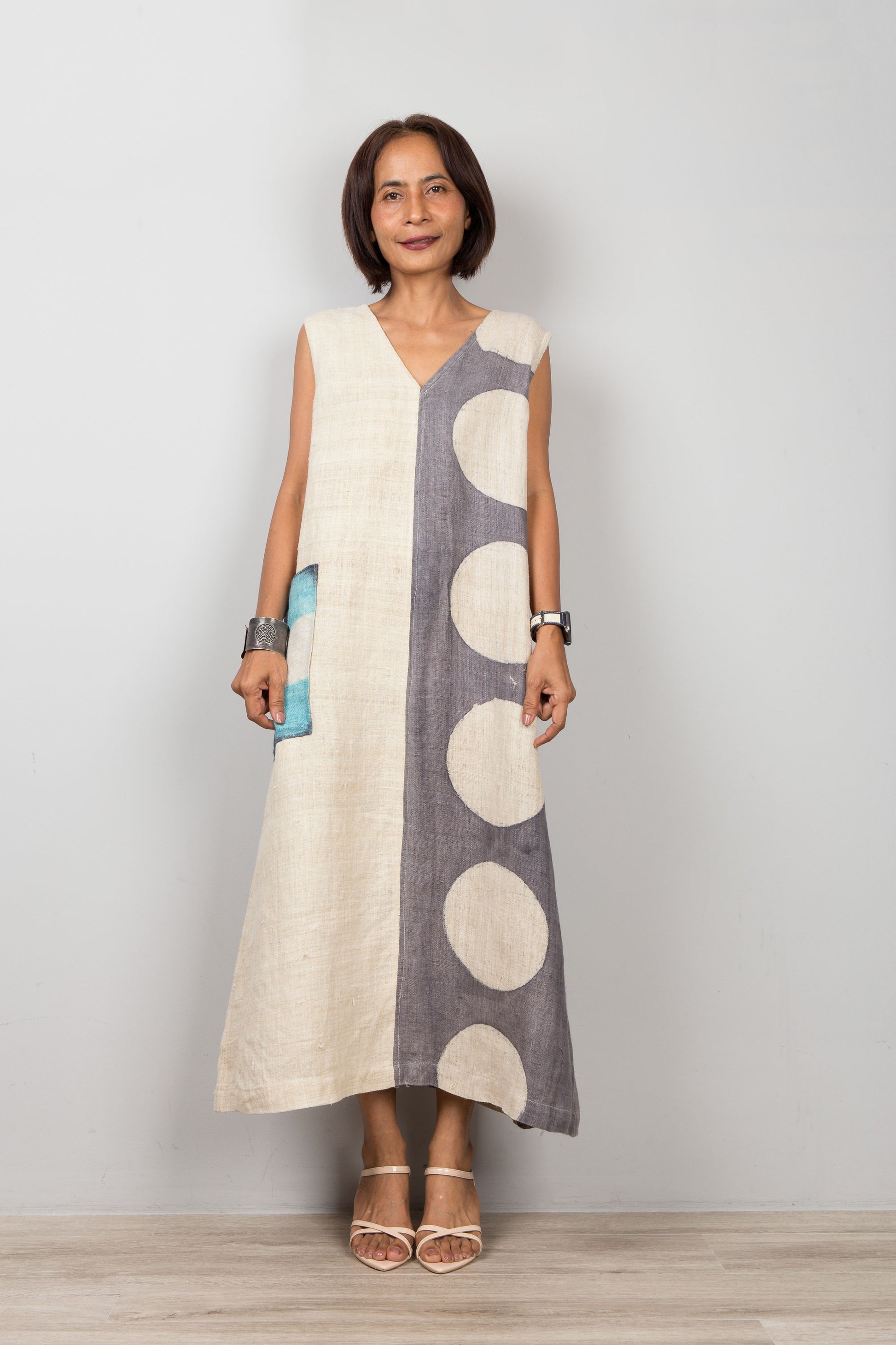 Woman wearing a sleeveless dress with a white and gray pattern on a plain background