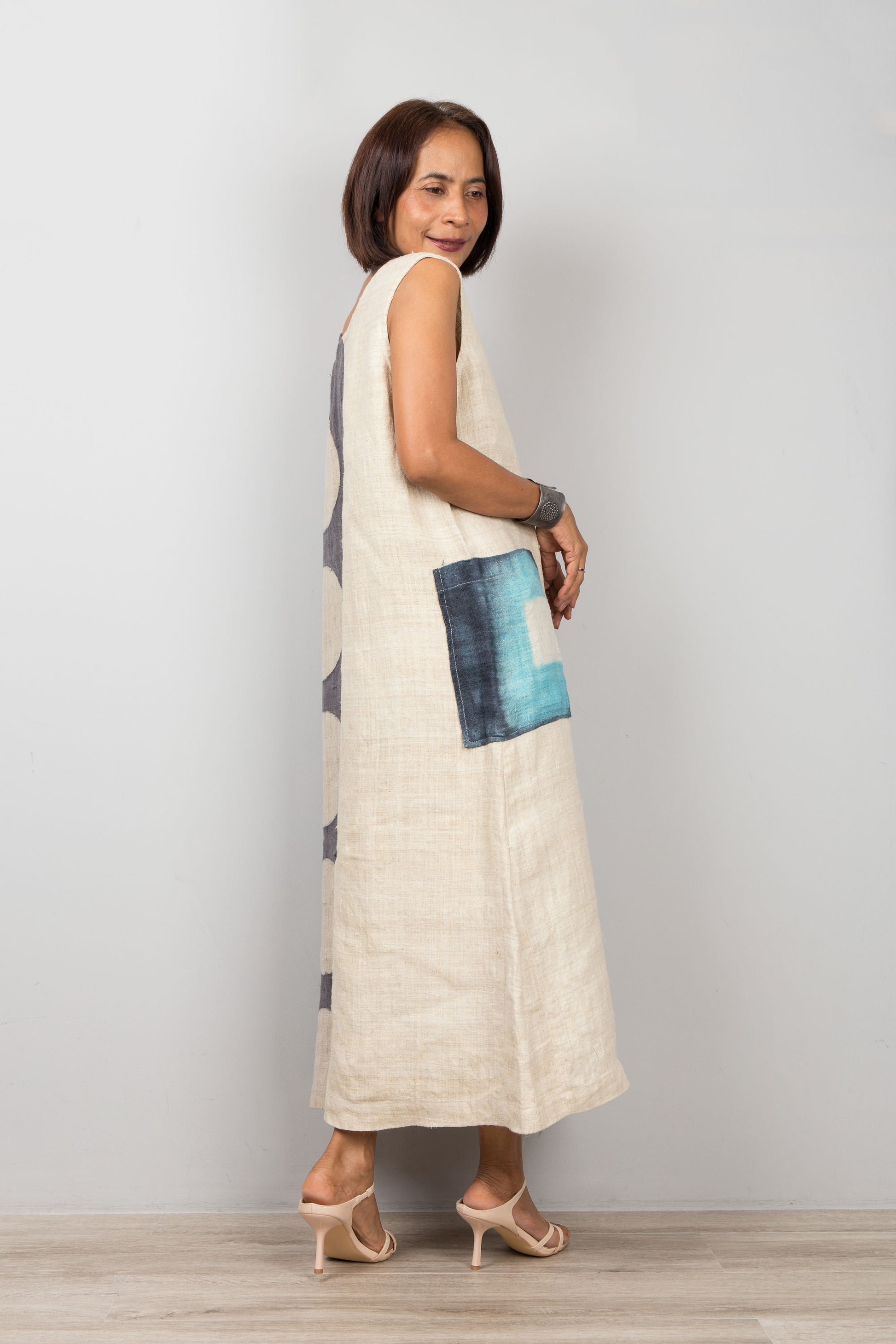 Woman wearing a long, light-colored dress with a blue pocket on a plain background