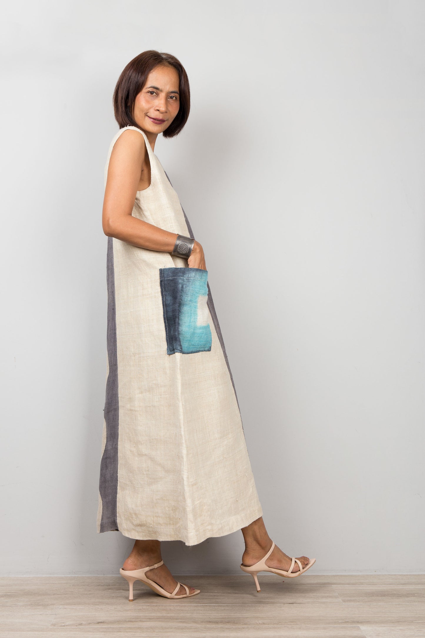 Woman wearing a long, light-colored hemp dress with shibori tie dye accents against a plain background
