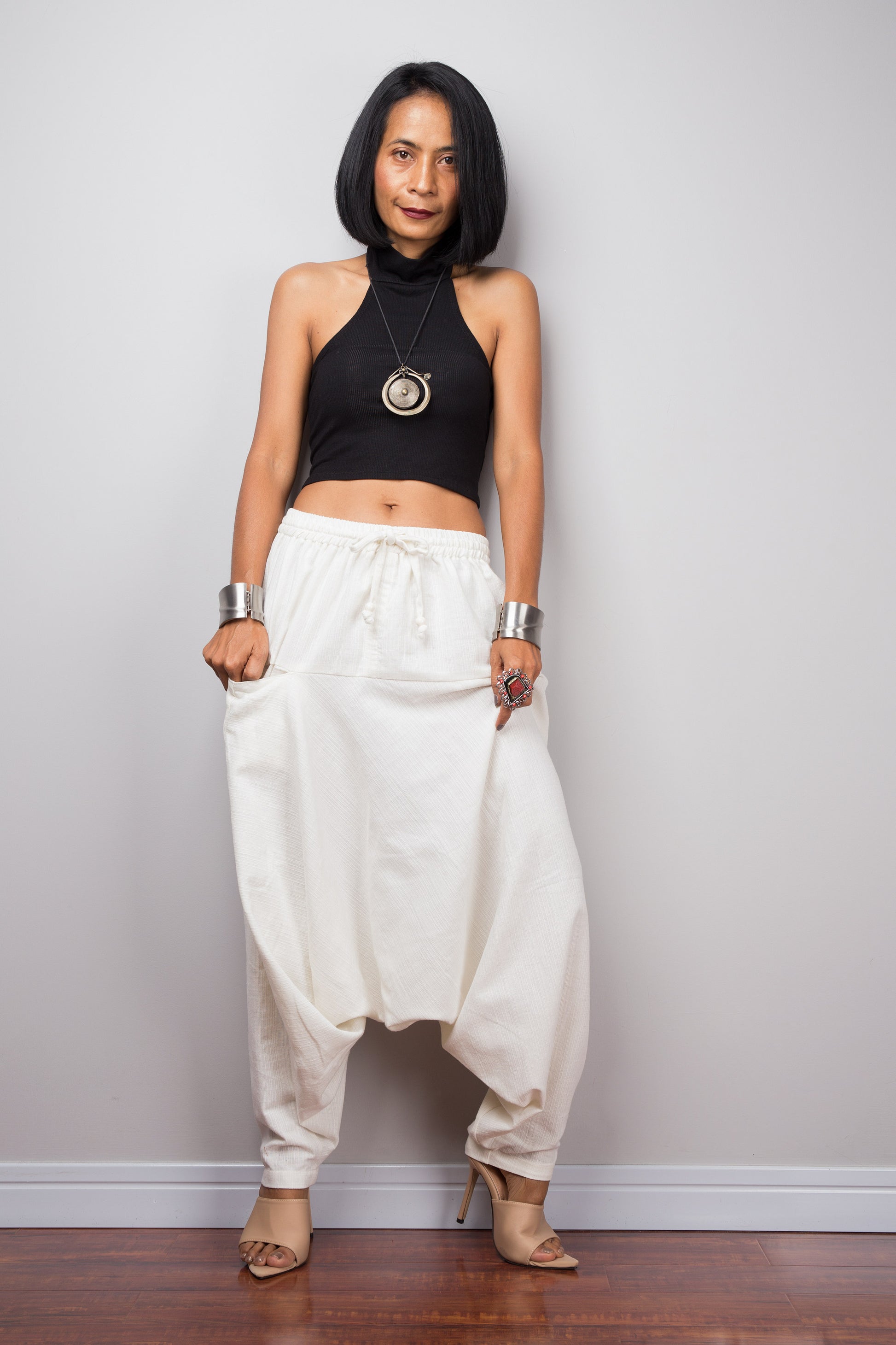 Model wearing off white harem pants with a loose fit, standing against a plain background, showcasing the full-length view.