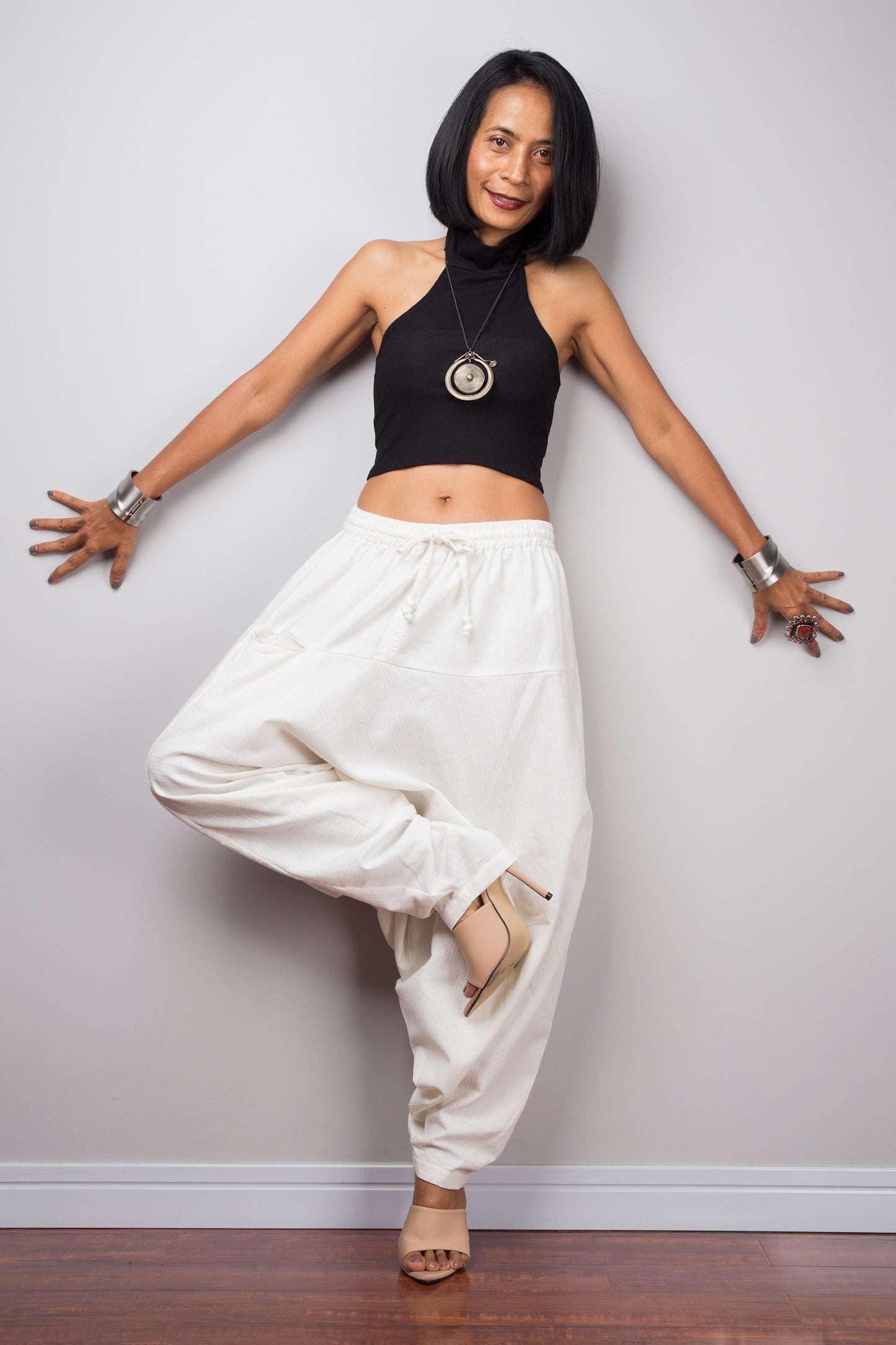 Model wearing brown harem pants with a loose fit, standing in lotus pose against a plain background, showcasing the full-length view.