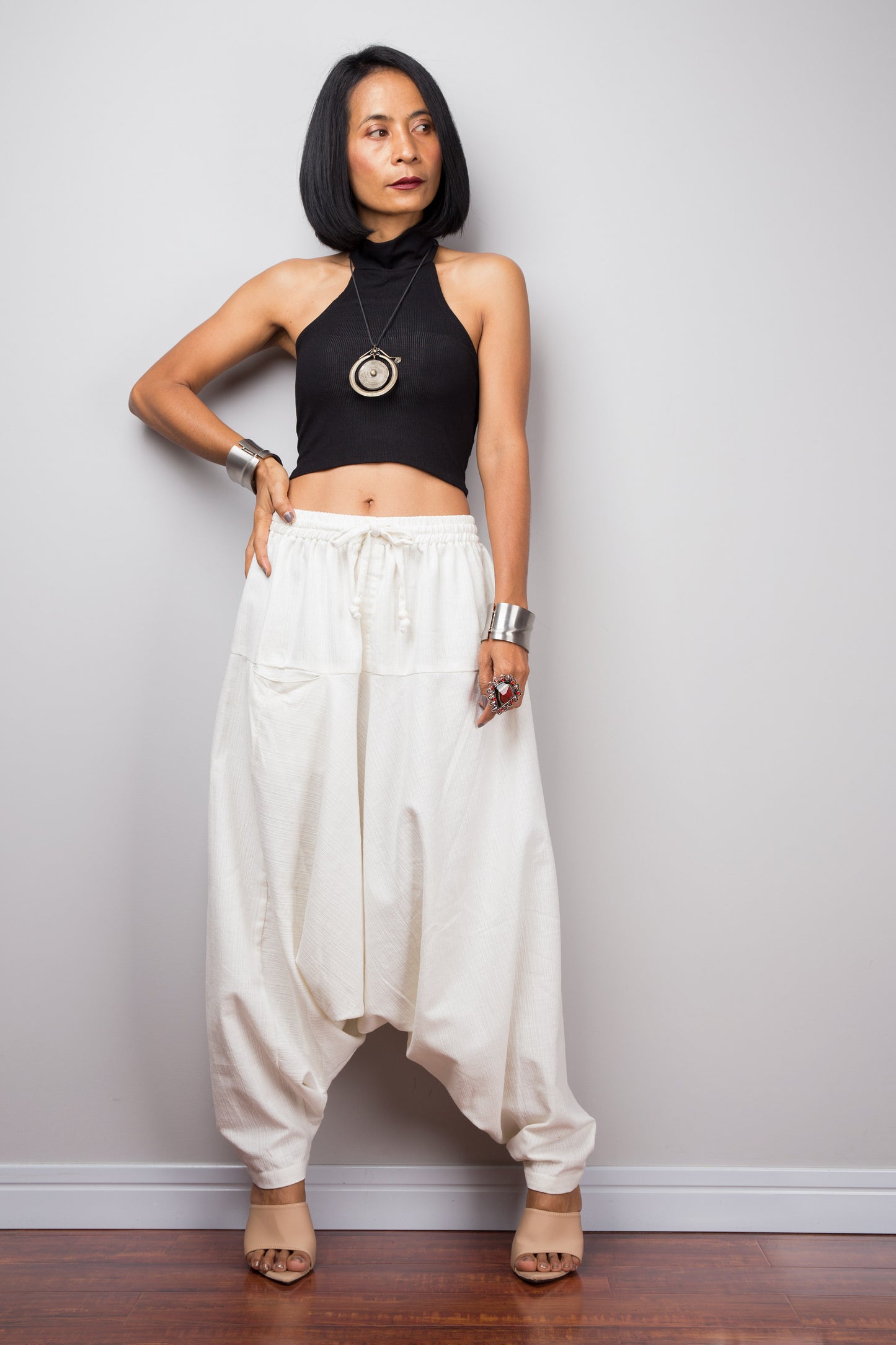 Model wearing off white cotton harem pants with a loose fit, standing against a plain background, showcasing the full-length view and pockets