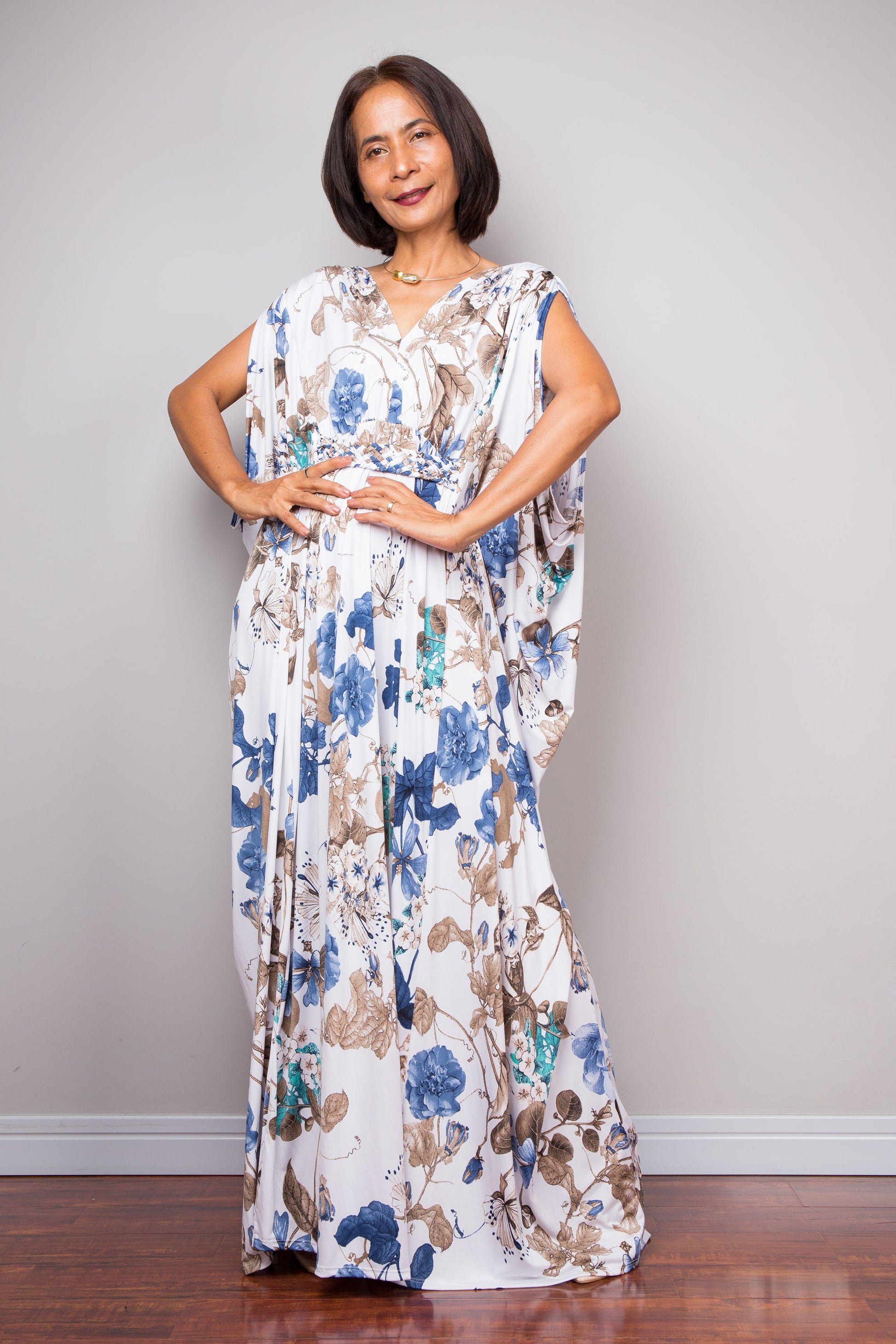 Woman wearing white floral caftan maxi dress with blue and brown flower print.