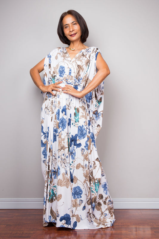 Woman wearing white floral caftan maxi dress with blue and brown flower print.