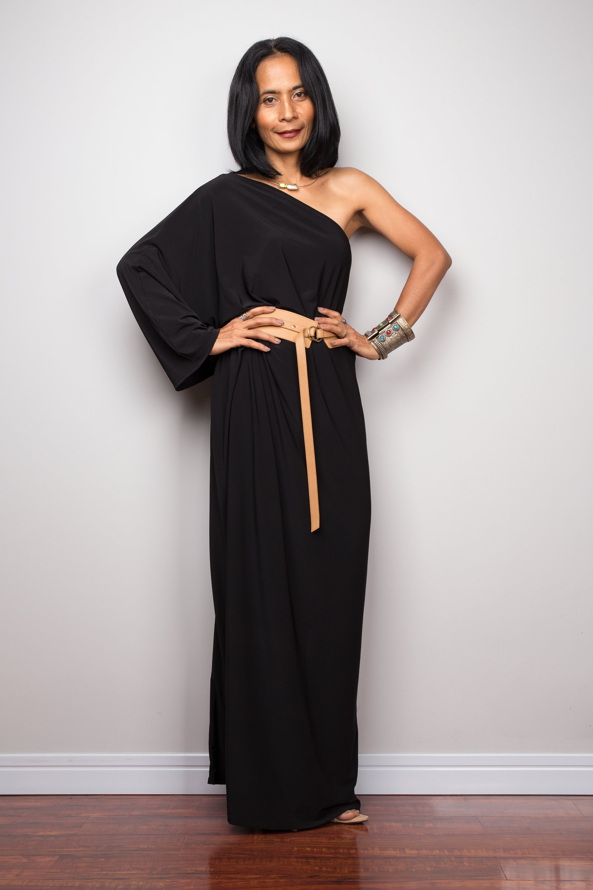 Black one shoulder kaftan dress paired with a light leather belt.