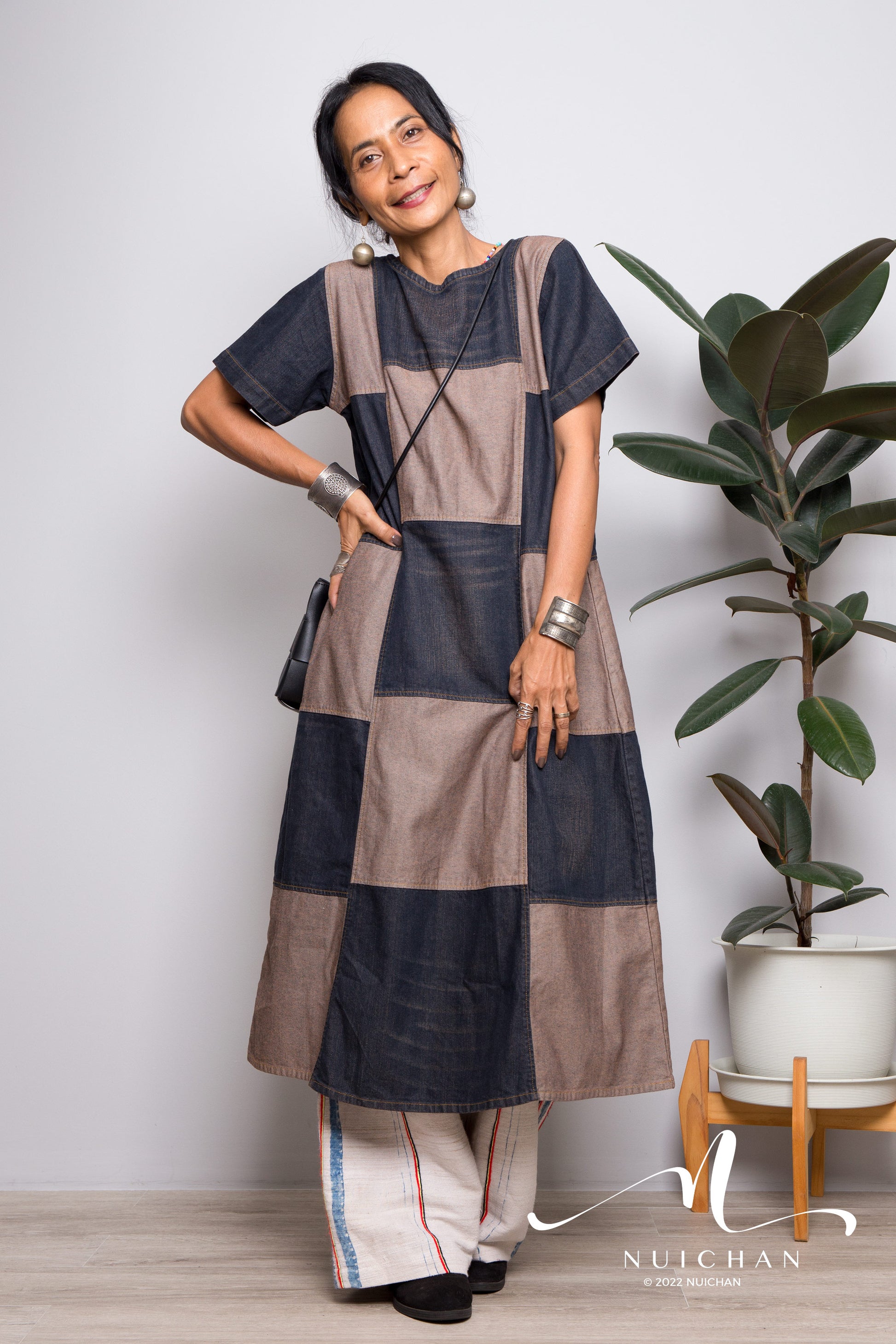 Model wearing a denim patchwork mid-length dress with a boho stonewashed finish, featuring a two-tone short-sleeve design. This Nuichan dress, with its relaxed A-line fit, is perfect for summer outings in a natural setting.

