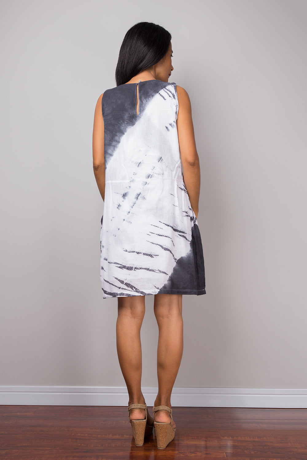 Model styling a shibori cotton dress with a black and white tie-dye pattern, paired with beige strappy heels and a statement ring. This sleeveless boho dress, photographed on a wooden floor indoors, offers a chic, sustainable look.


