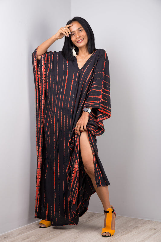 A woman posing in a long black tie-dye kaftan dress with orange streaks, 