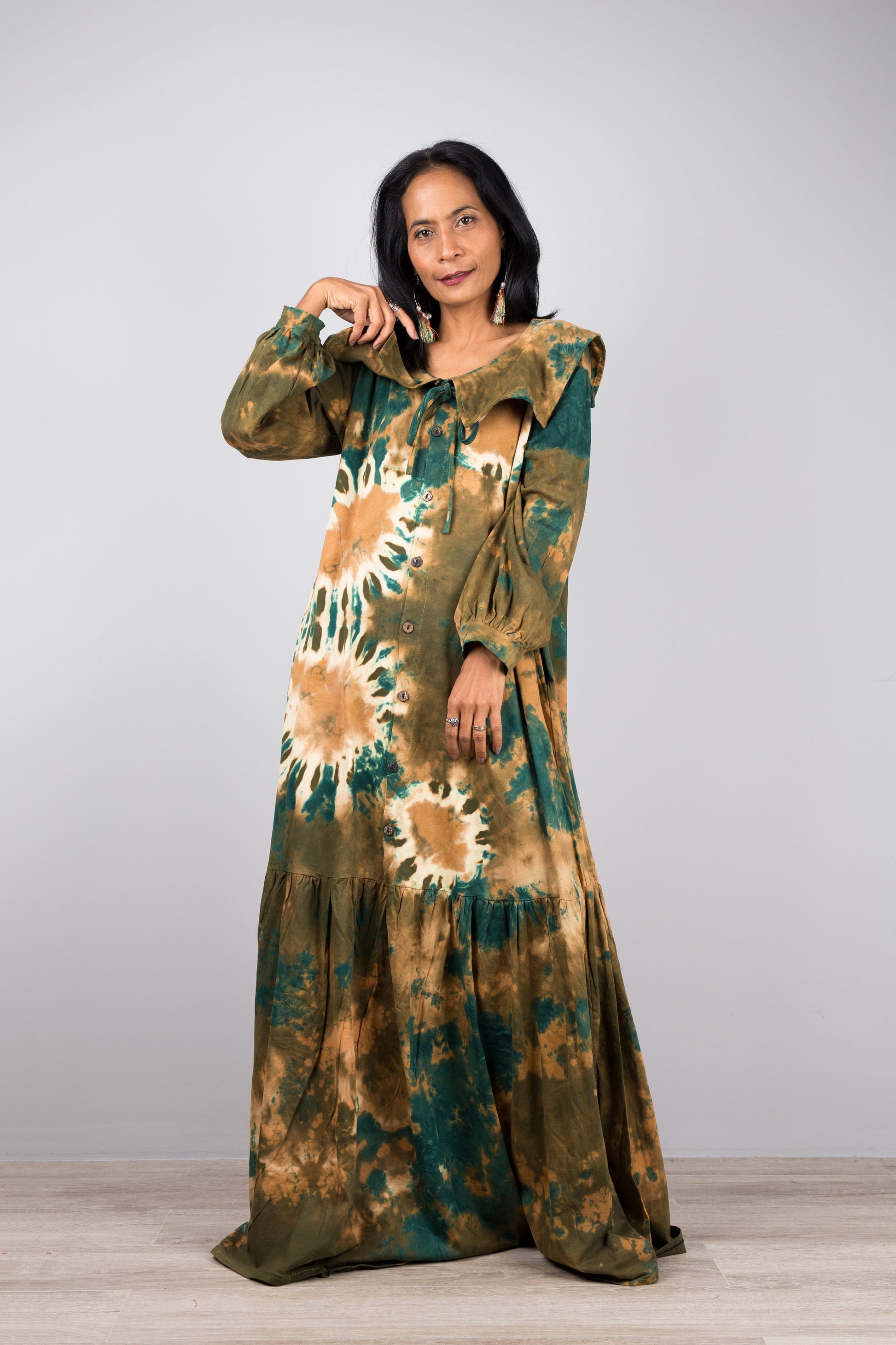 Green tie-dye kaftan maxi dress with navy collar and long sleeves on a woman, featuring a flowing silhouette, set against a minimalist gray and wood background, with nude sandals.

