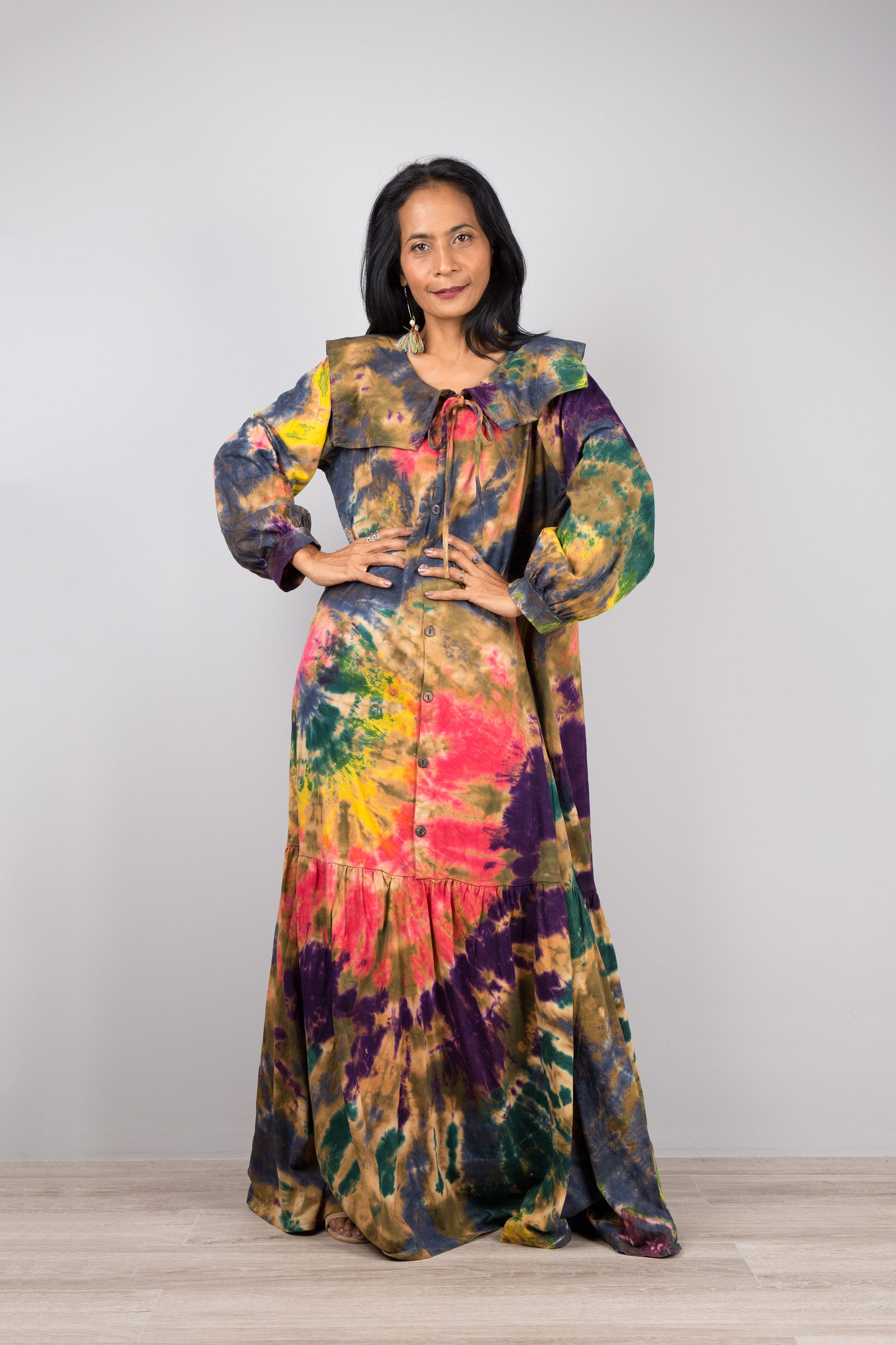 Elegant tie-dye kaftan maxi dress with a navy-trimmed collar and gathered sleeves, worn by a woman against a gray wall and wooden floor, paired with nude sandals and earrings

