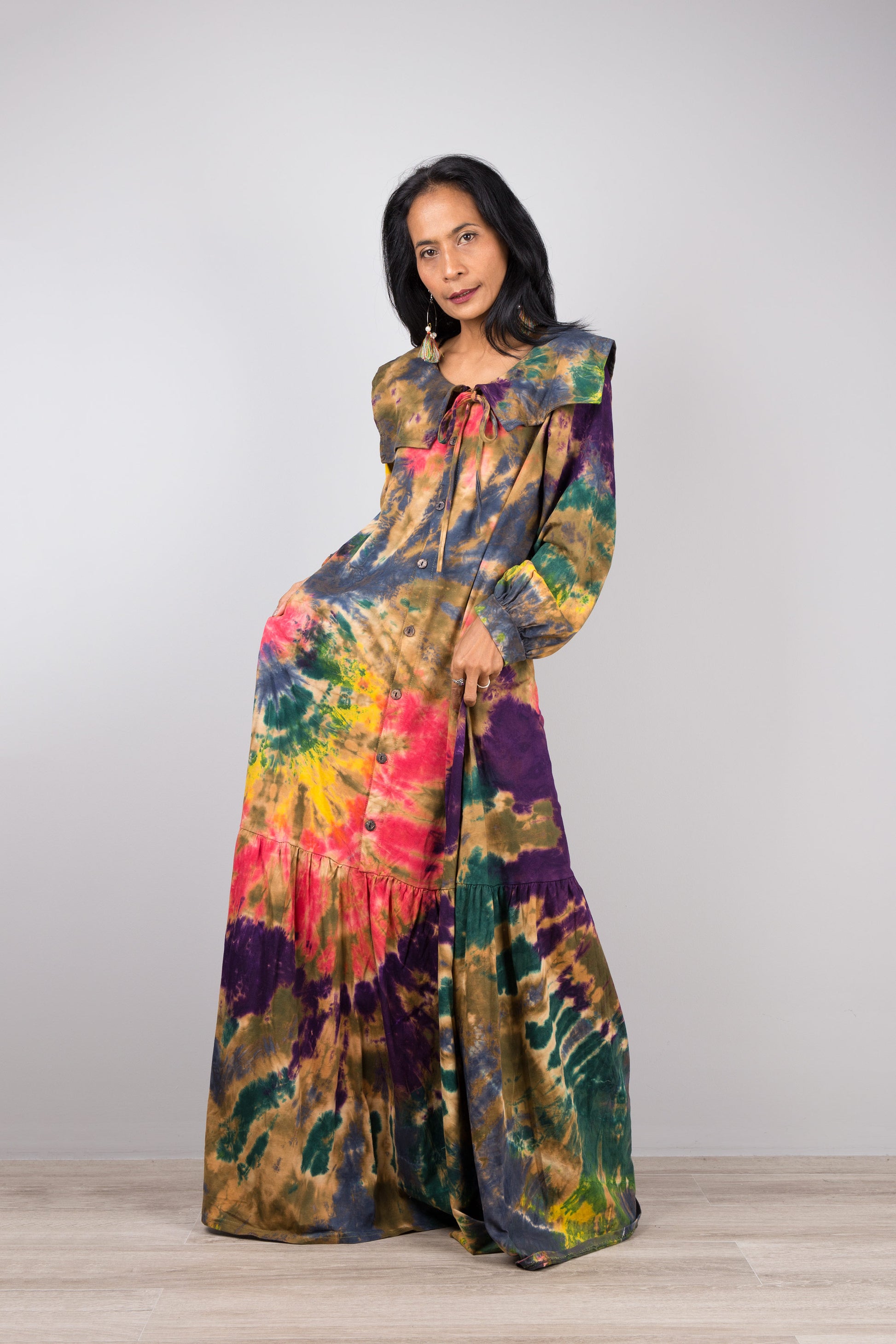 tie-dye kaftan maxi dress with navy collar and long sleeves on a woman, featuring a flowing silhouette, set against a minimalist gray and wood background, with nude sandals.

