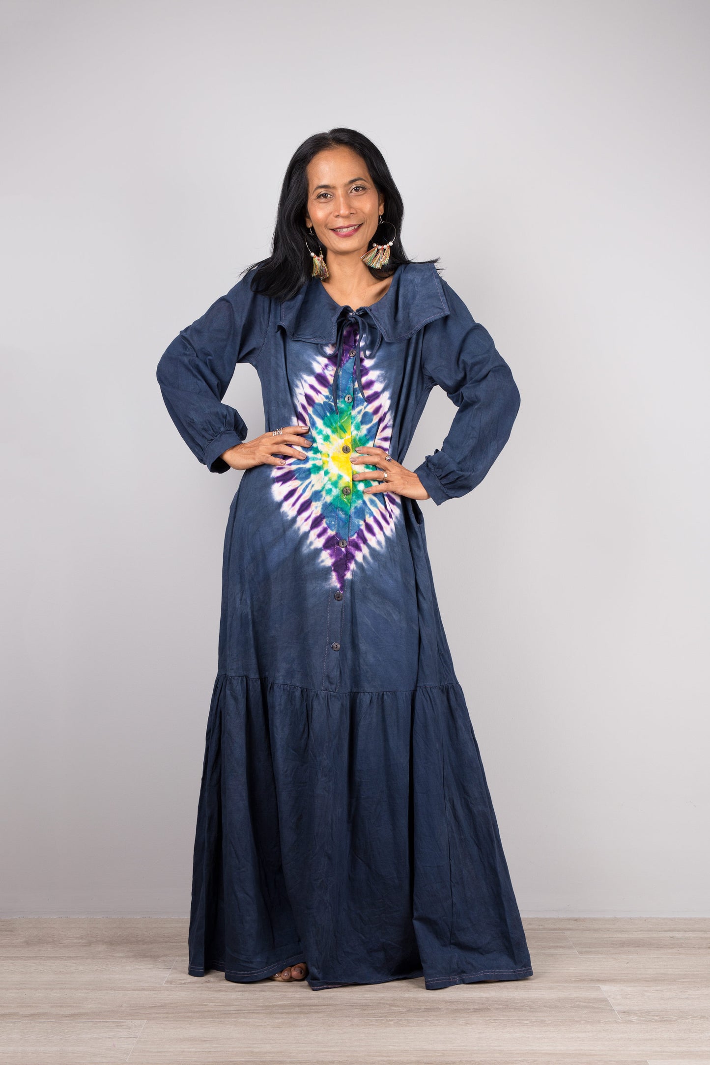 Dark blue tie-dye kaftan maxi dress with navy collar and long sleeves on a woman, featuring a flowing silhouette, set against a minimalist gray and wood background, with nude sandals

